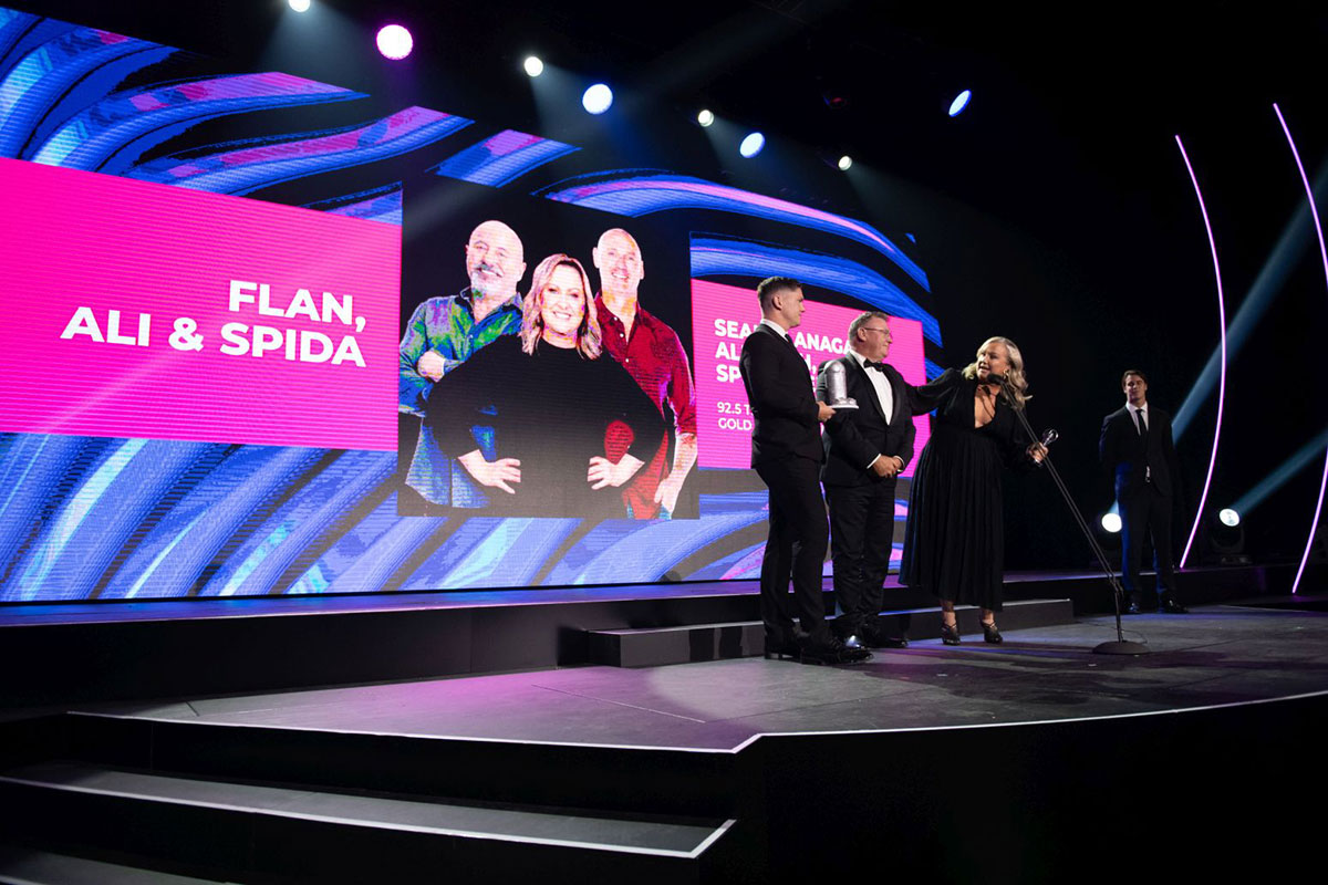 Ali Plath on stage accepting the ACRA for Best On Air Team, Provincial, with Flan, Ali & Spida on the big screen